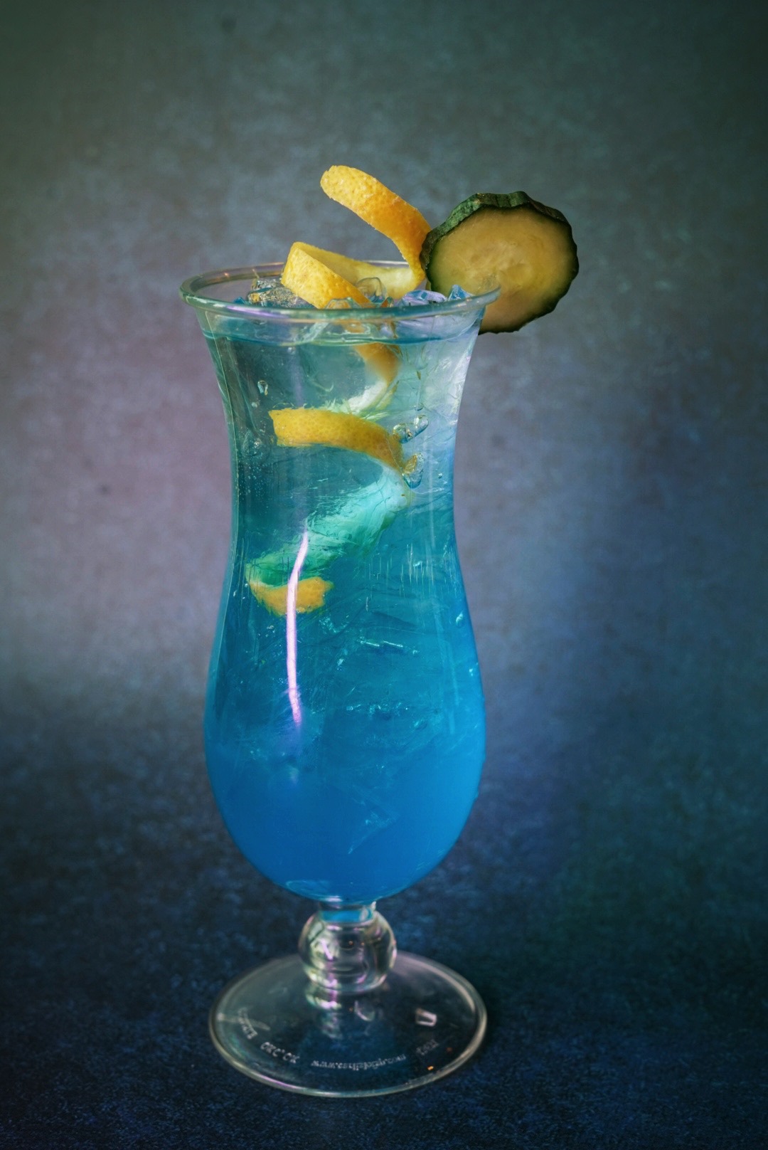 Signature blue cocktail with citrus twist and cucumber garnish
